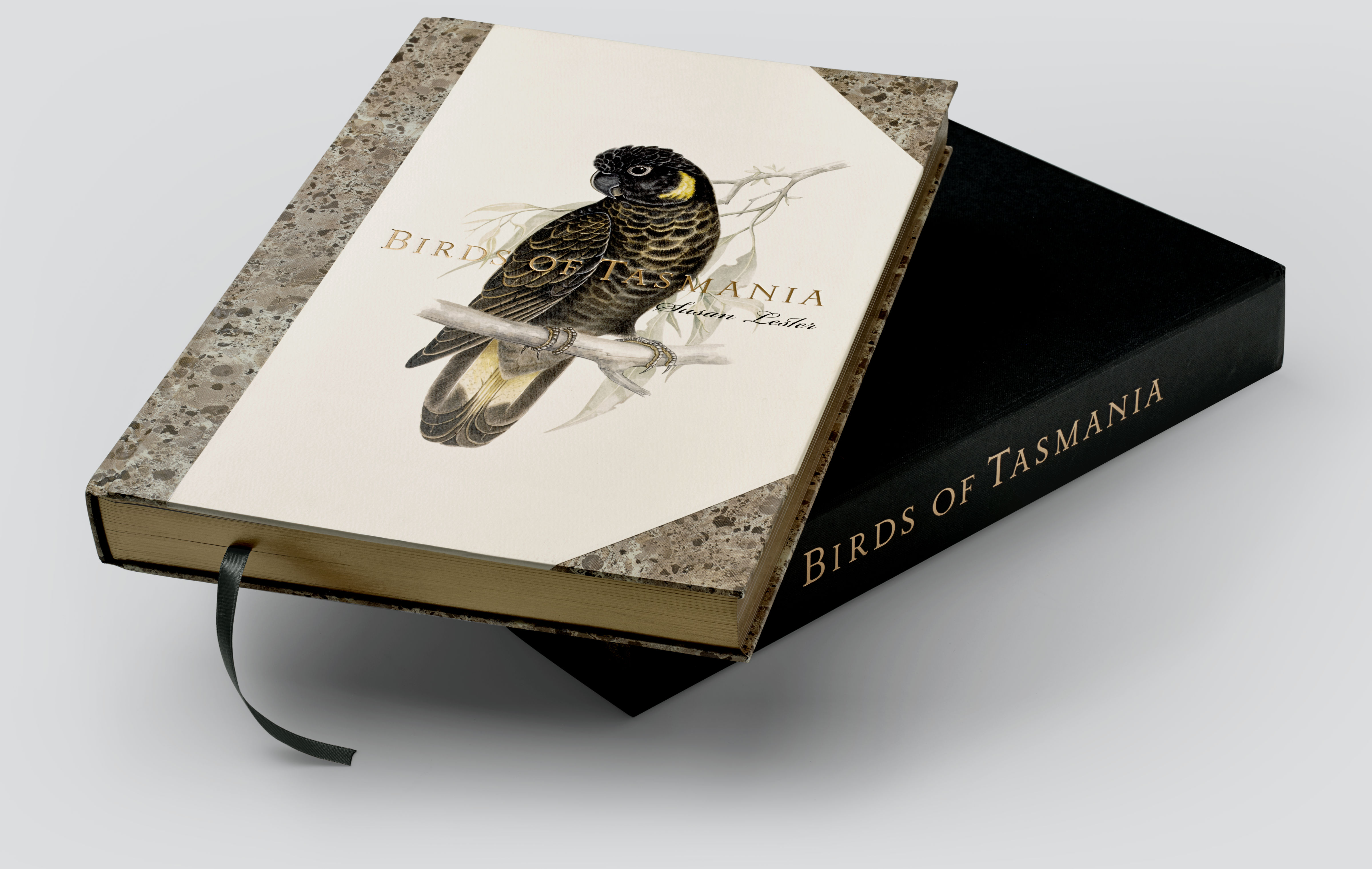The ‘Birds of Tasmania’ by Susan Lester book, with a Yellow-tailed Cockatoo image and gold and black foil titling, sitting on the black clamshell presentation box.