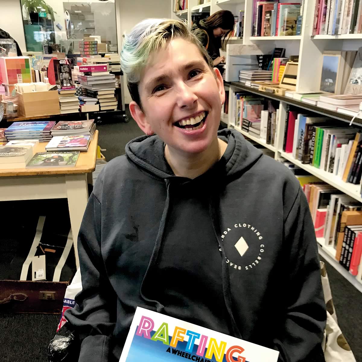 Portrait photo of author/artist Janelle McMillan holding her book Rafting – A Wheelchair Won’t Stop Us! Photo: Michael Small.