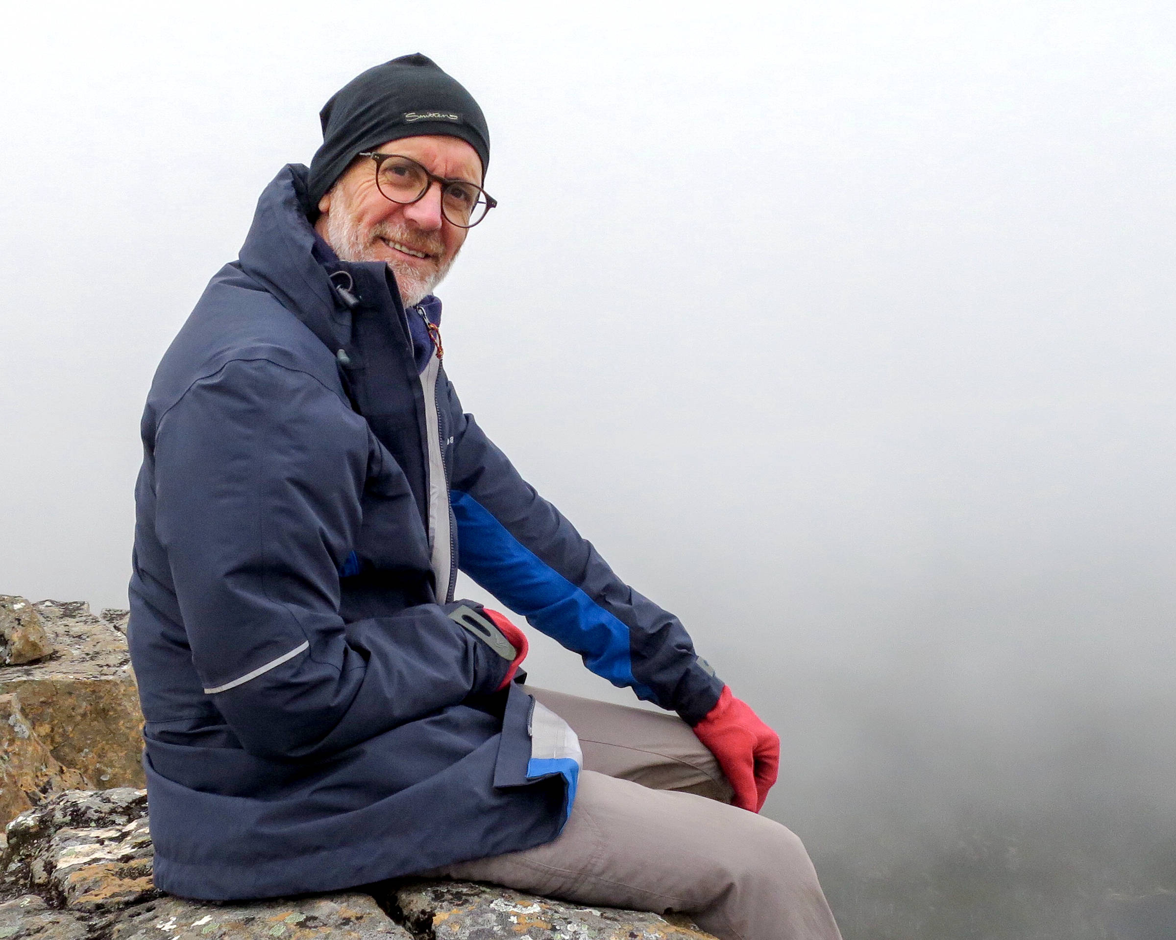 A portrait image of author Ian Terry sitting on a rock ledge in the mist. Photograph by Erica Burgess.