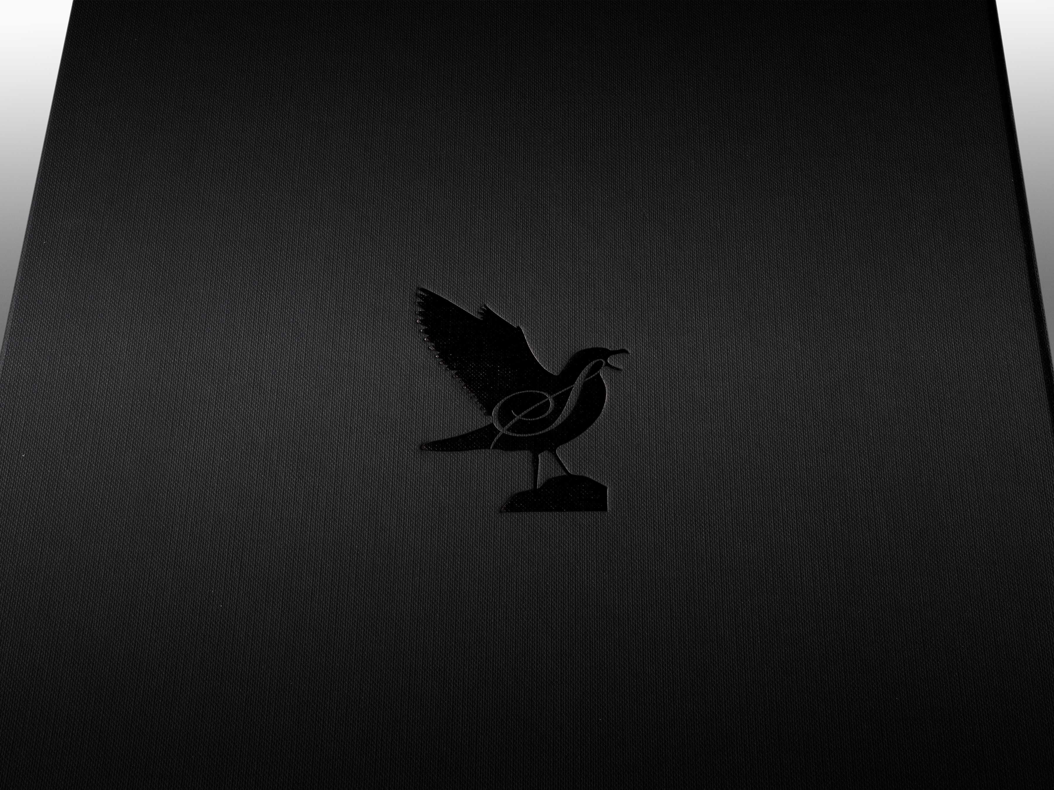 A close-up of the black embossed symbol of a bird with the letter ‘S’ in a script font.